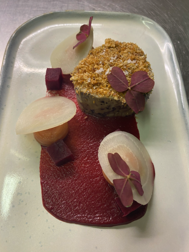 Dessert élégant avec gâteau, sauce framboise et garnitures florales décoratives.